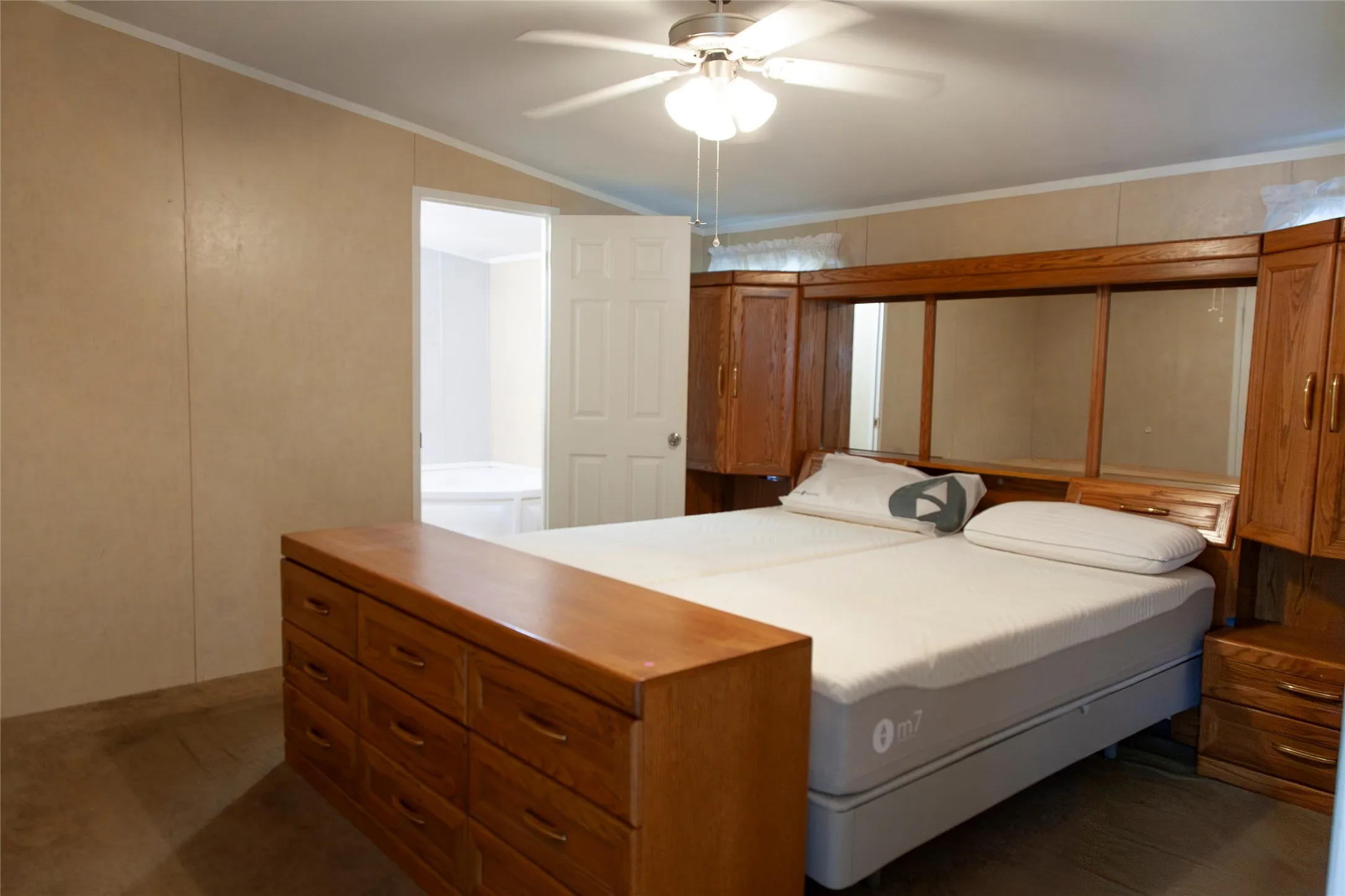 Spacious sleeping area featuring built-in wood cabinetry, a ceiling fan, and light-toned wall paneling
