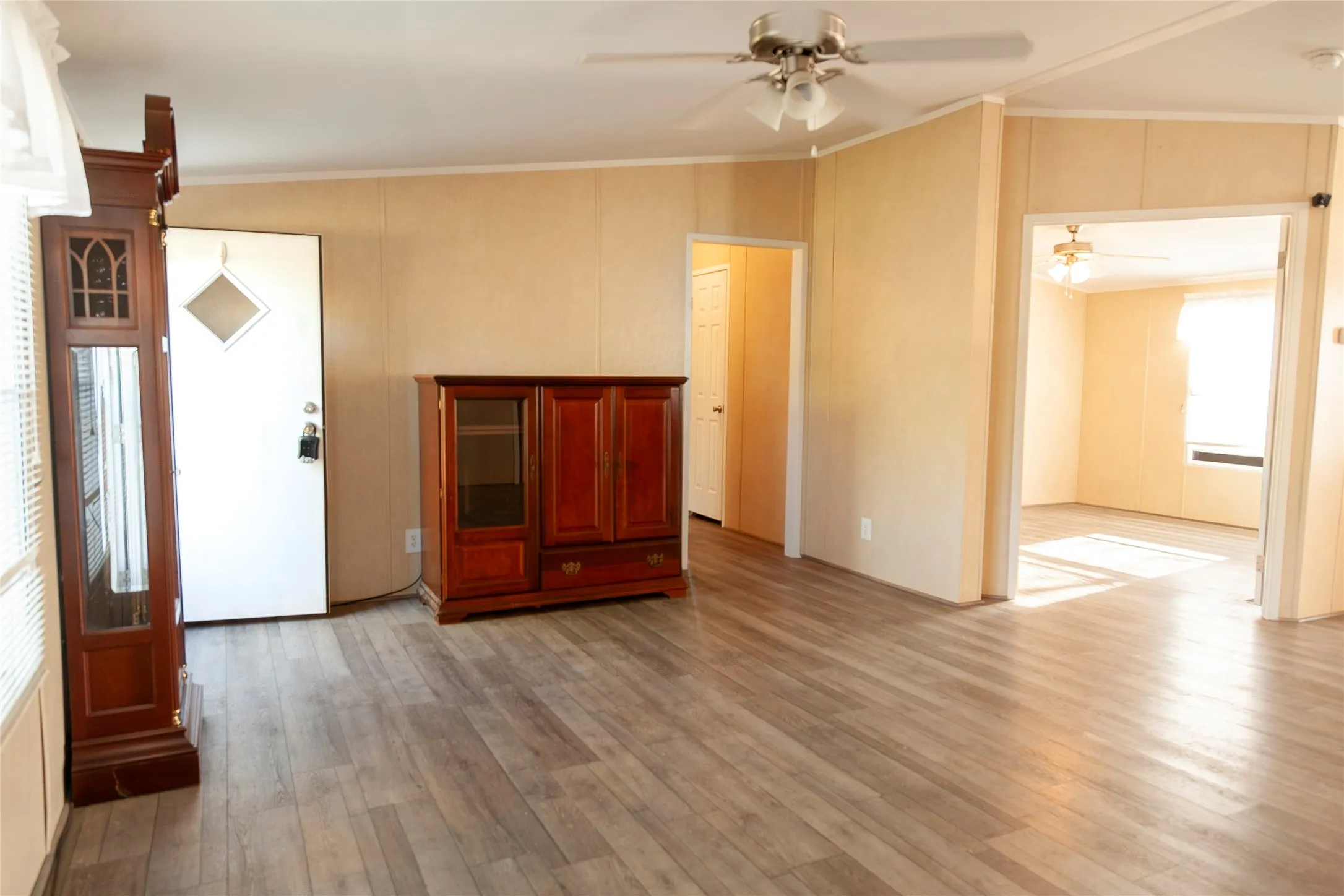 Spacious living area featuring wood-finish flooring, a ceiling fan with integrated lighting, and neutral wall paneling