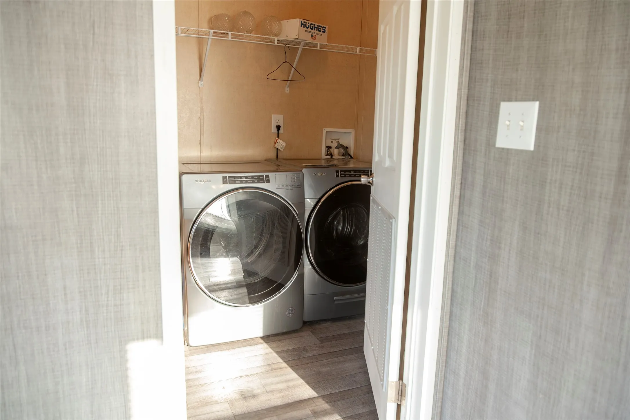 Dedicated laundry area featuring a shelf system and wood-finish flooring
