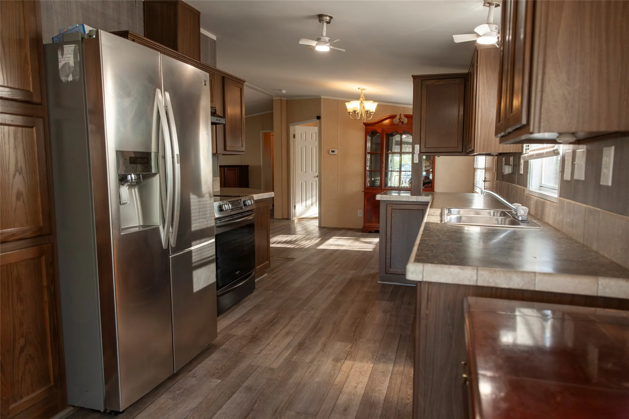 Kitchen featuring wood-finish flooring, stainless steel French door refrigerator, black range, tile countertops, and dark wood-tone cabinetry