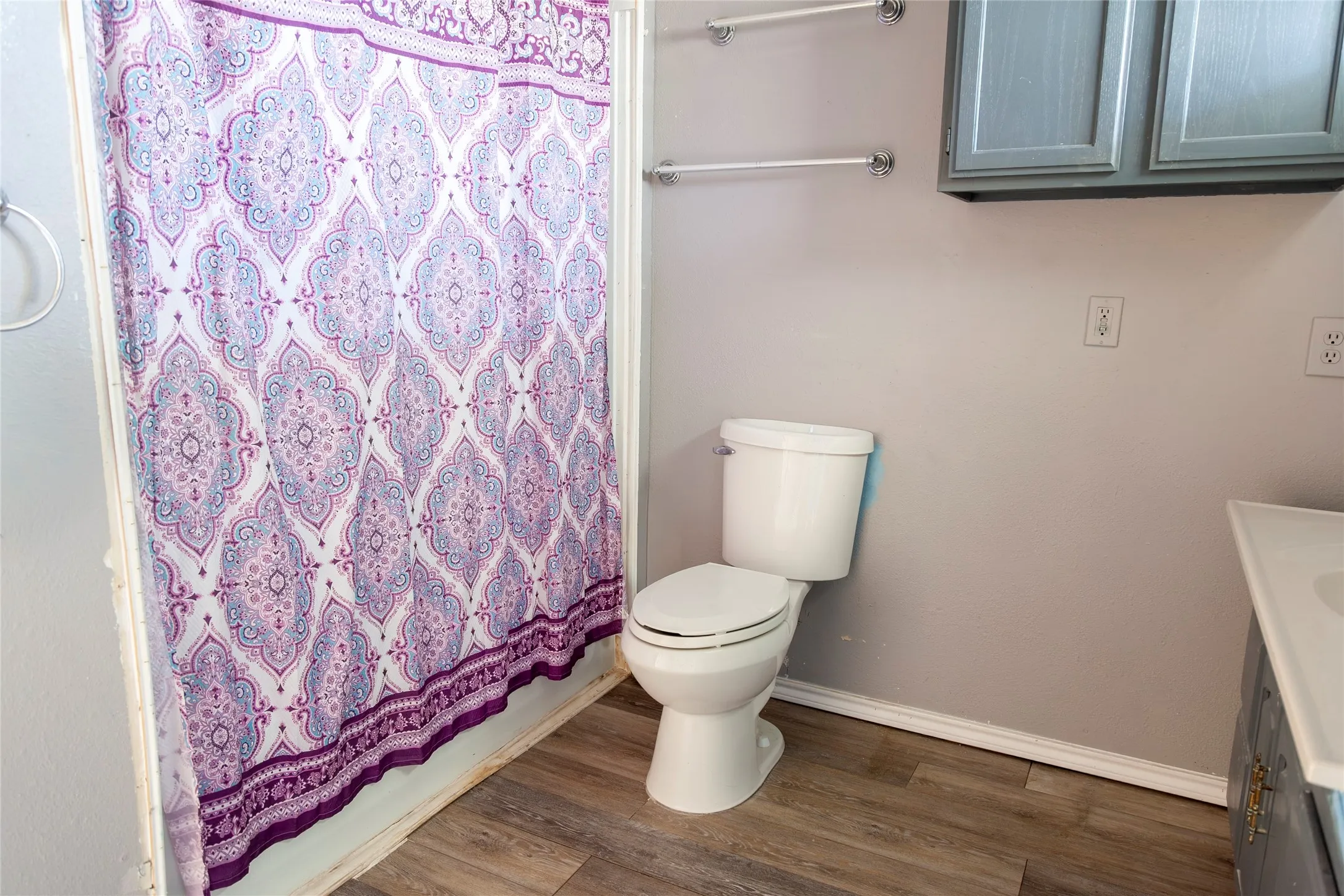 Bathroom featuring wood-finish flooring, a white toilet, and light gray walls