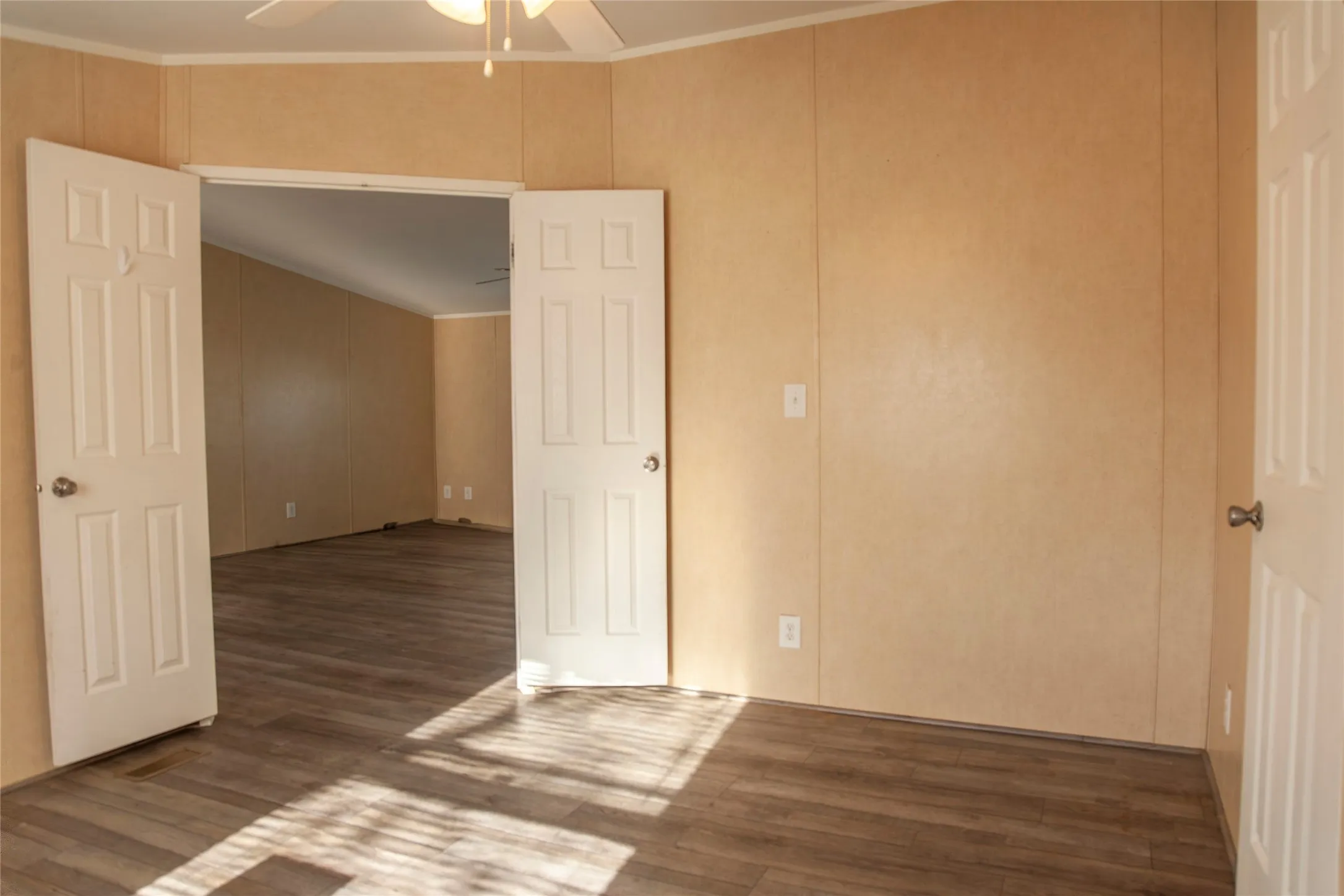 Spacious interior room featuring wood-finish flooring, neutral wall finishes, and a ceiling fan with light fixture