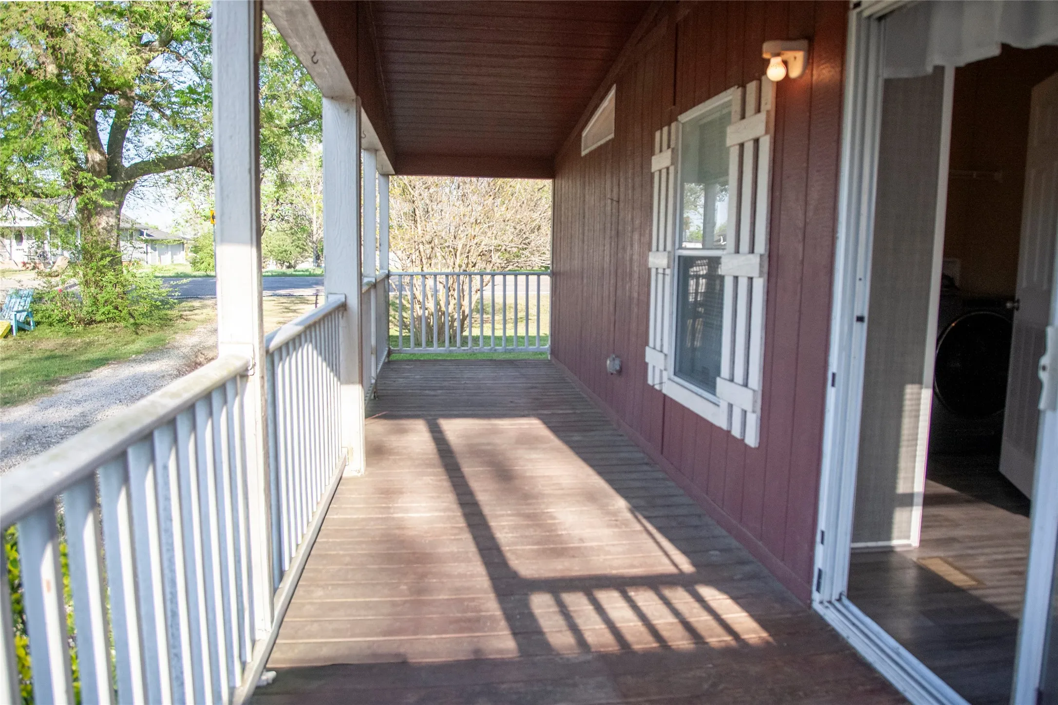 Covered wood-finish porch featuring white support columns and railings, a window with white shutters, and a sliding glass door entry