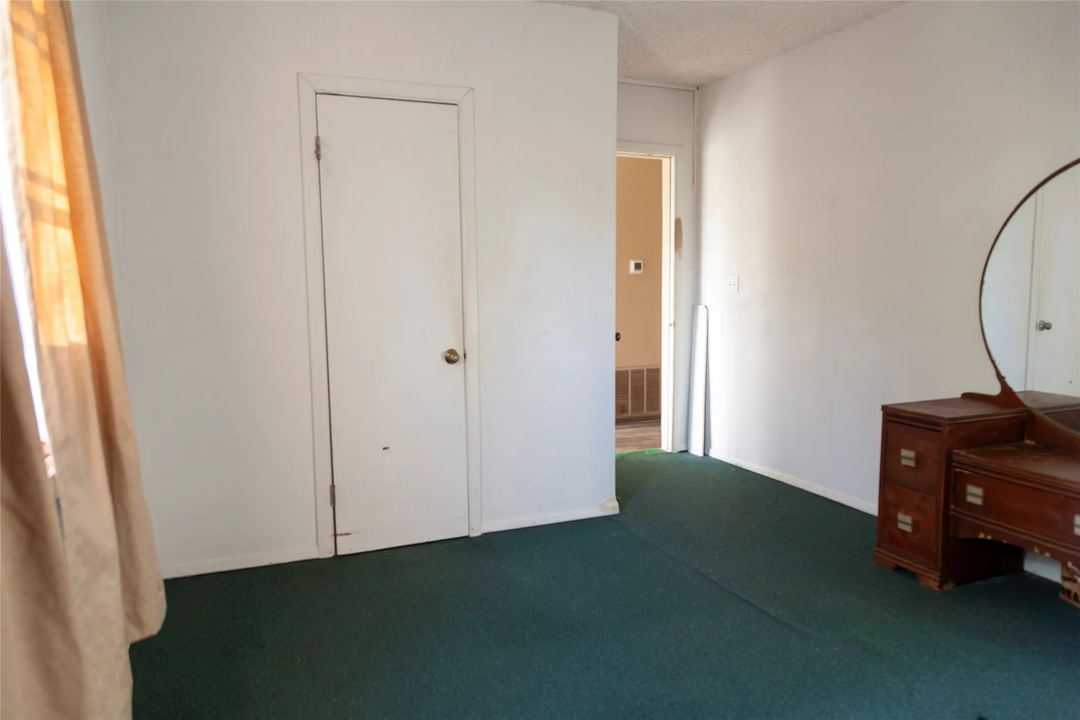 Room featuring white walls, green carpeting, and a white door with a round brass-tone doorknob