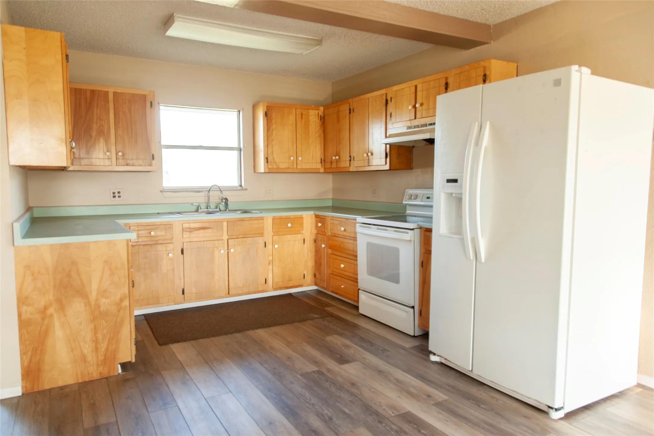 Kitchen featuring wood-finish flooring, light wood cabinetry, white appliances, and a window above the sink
