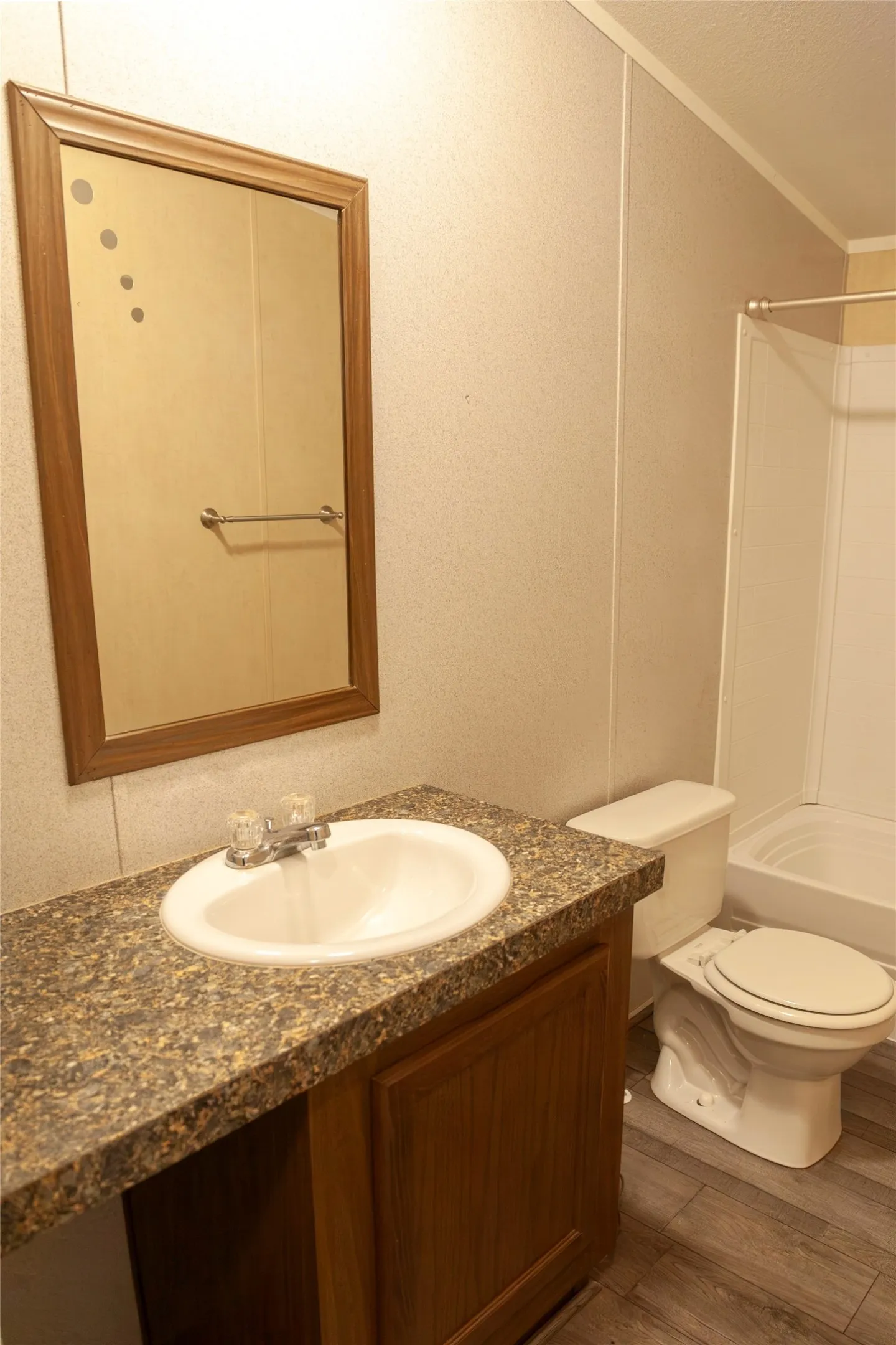 Bathroom featuring a wood-finish vanity with a built-in sink, speckled countertop, and wall-mounted mirror