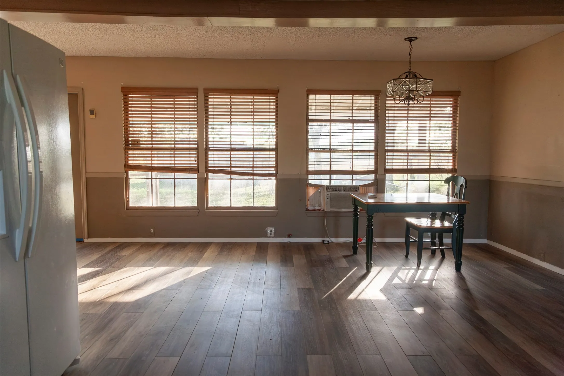 Open-concept room featuring wood-finish flooring, three windows with blinds, a two-tone wall finish, and a decorative overhead light fixture