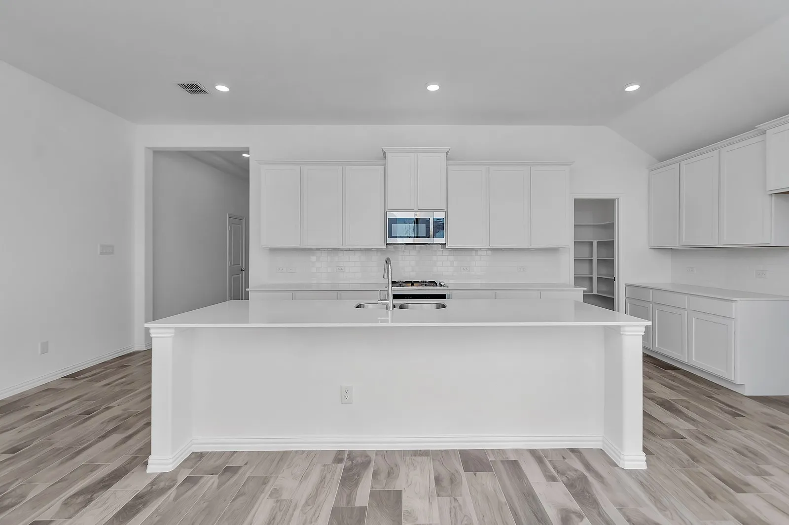 Kitchen with stainless steel microwave, a kitchen island with sink, decorative backsplash, light countertops, and lofted ceiling
