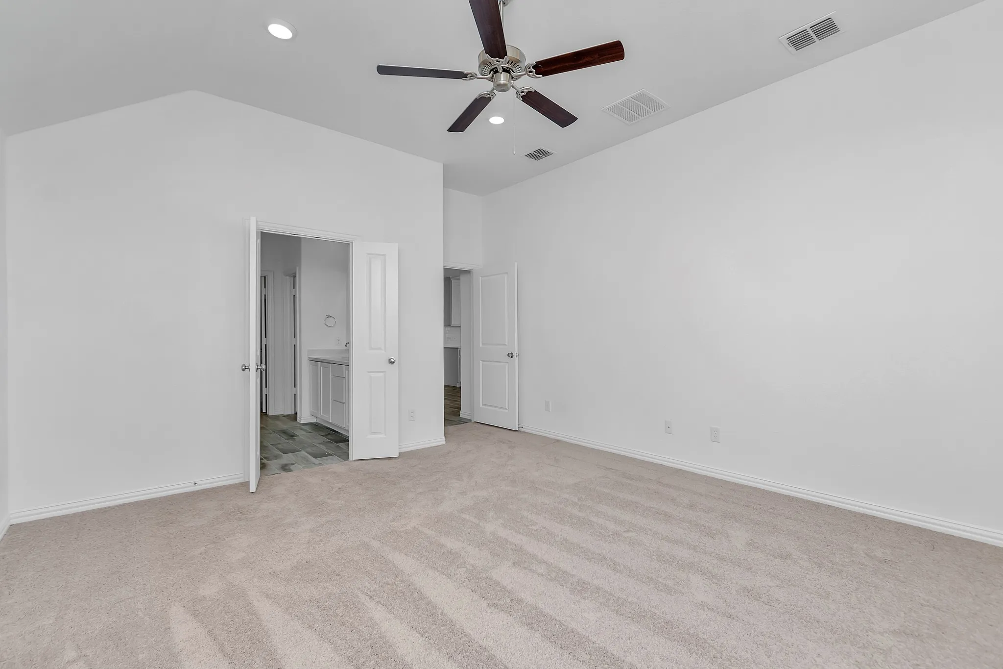 Unfurnished bedroom featuring light colored carpet, recessed lighting, lofted ceiling, connected bathroom, and ceiling fan