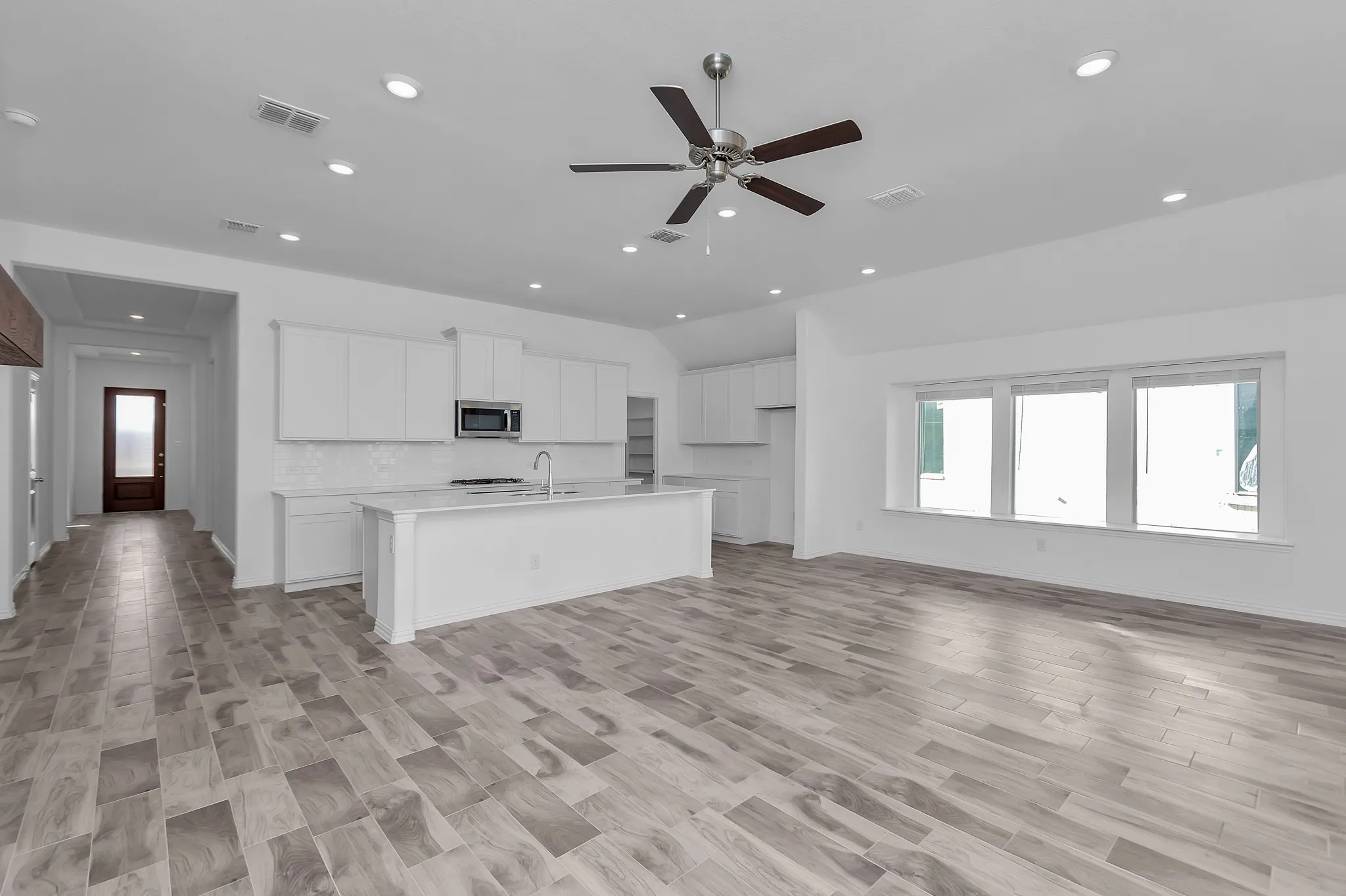 Kitchen featuring stainless steel microwave, lofted ceiling, recessed lighting, a ceiling fan, and an island with sink
