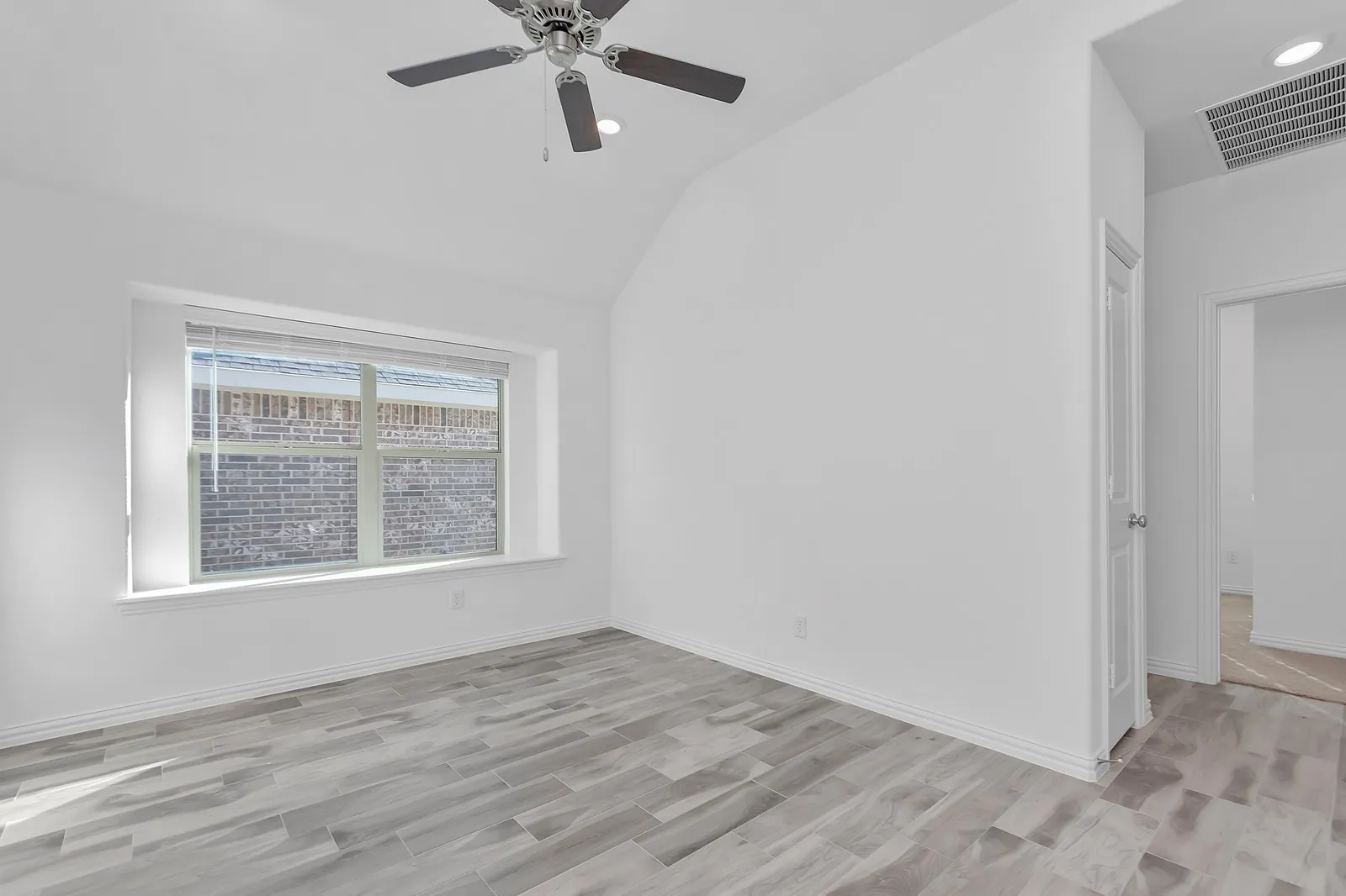 Spare room with light wood-type flooring, vaulted ceiling, and a ceiling fan