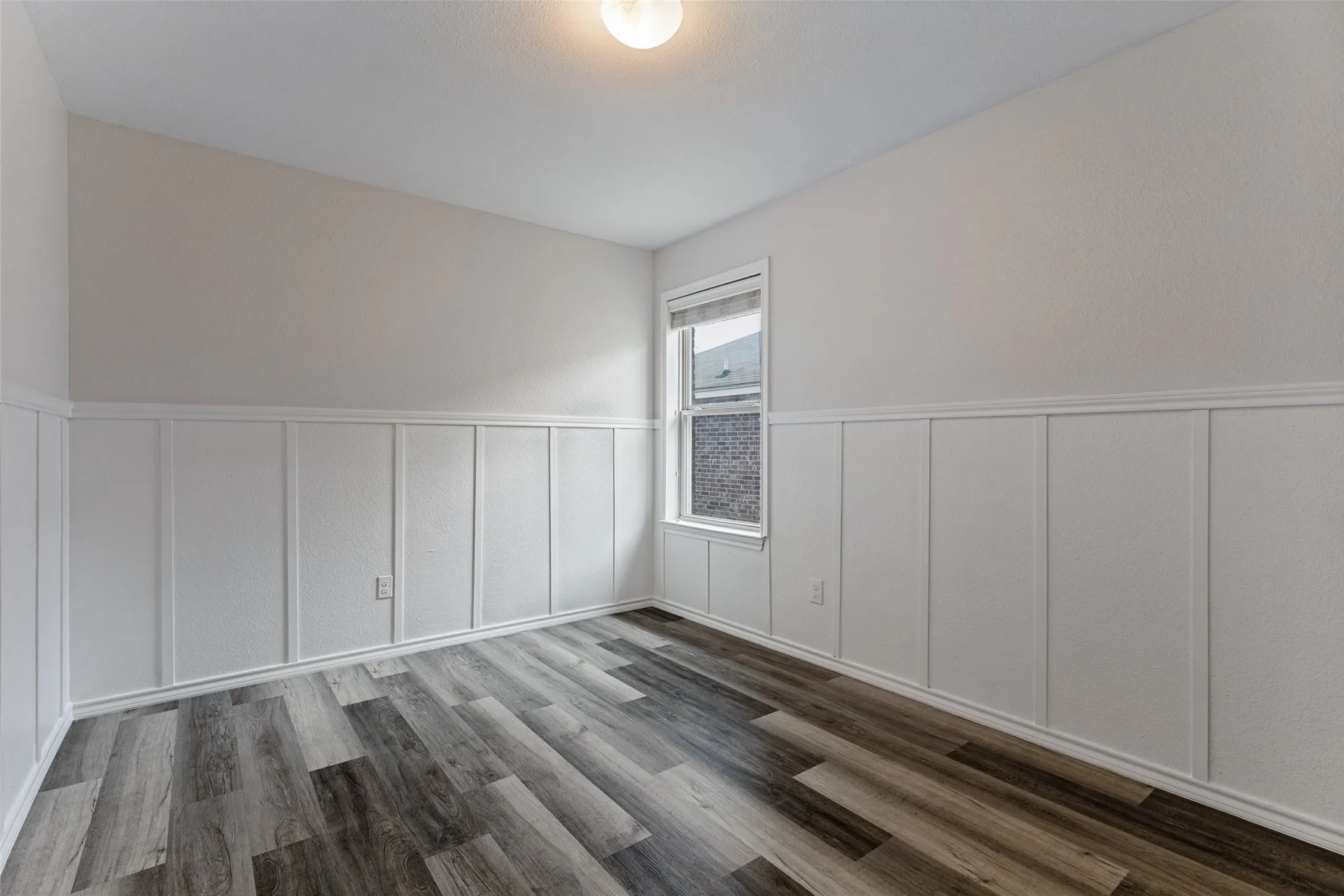 Wood-finish flooring, wainscoting with decorative trim, and a single window with blinds