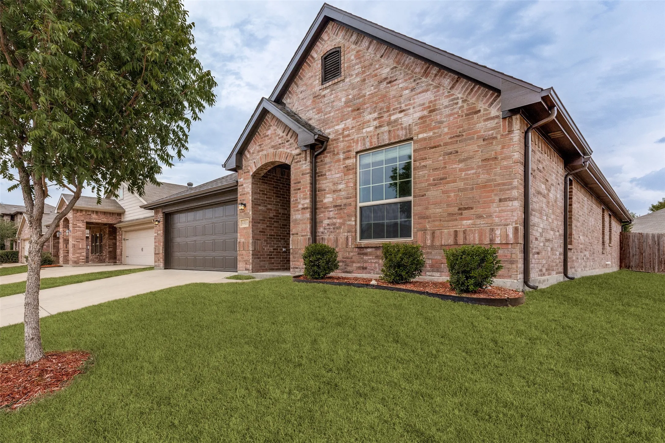 Brick exterior with arched entryway and gabled roofline, complemented by a manicured lawn with mature landscaping and professional hardscaping