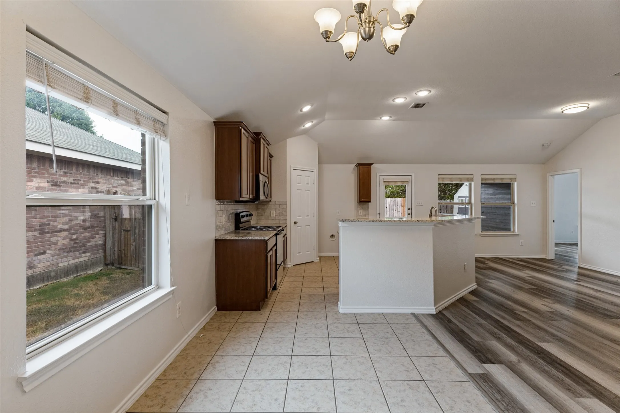 Open-concept living space featuring wood-finish flooring throughout, custom cabinetry with abundant storage, stainless steel appliances, tile countertops, and recessed lighting