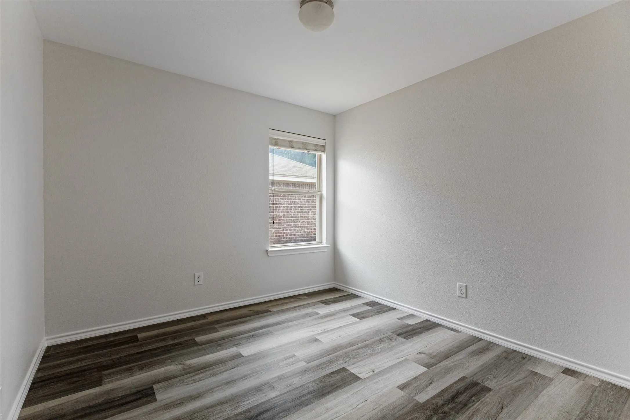 Bright corner bedroom featuring expansive windows with natural light, pristine white walls, and wood-finish flooring with mixed-width planks in warm gray and charcoal tones