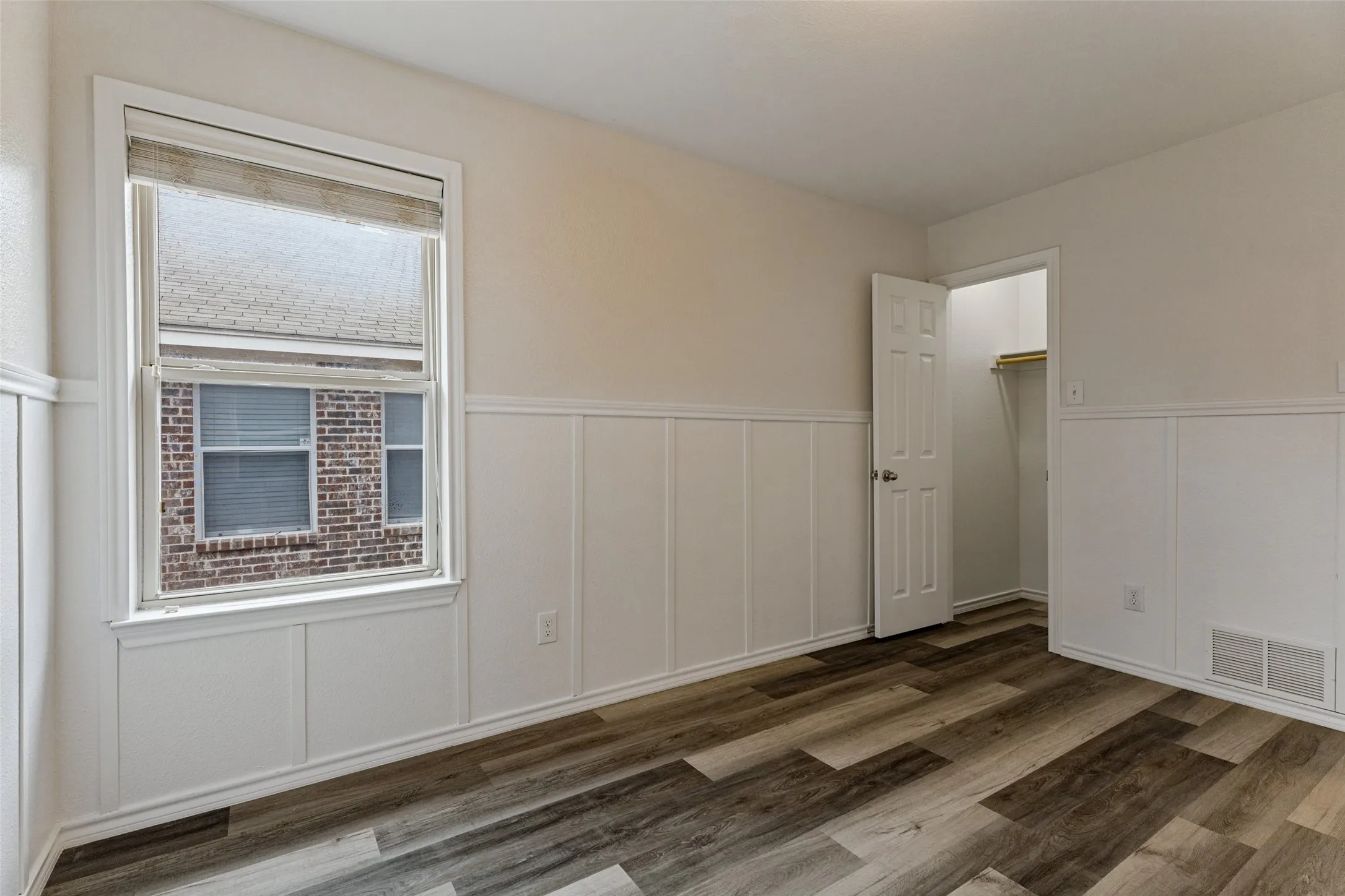 Wood-finish flooring, white paneled wainscoting, and a single window with blinds