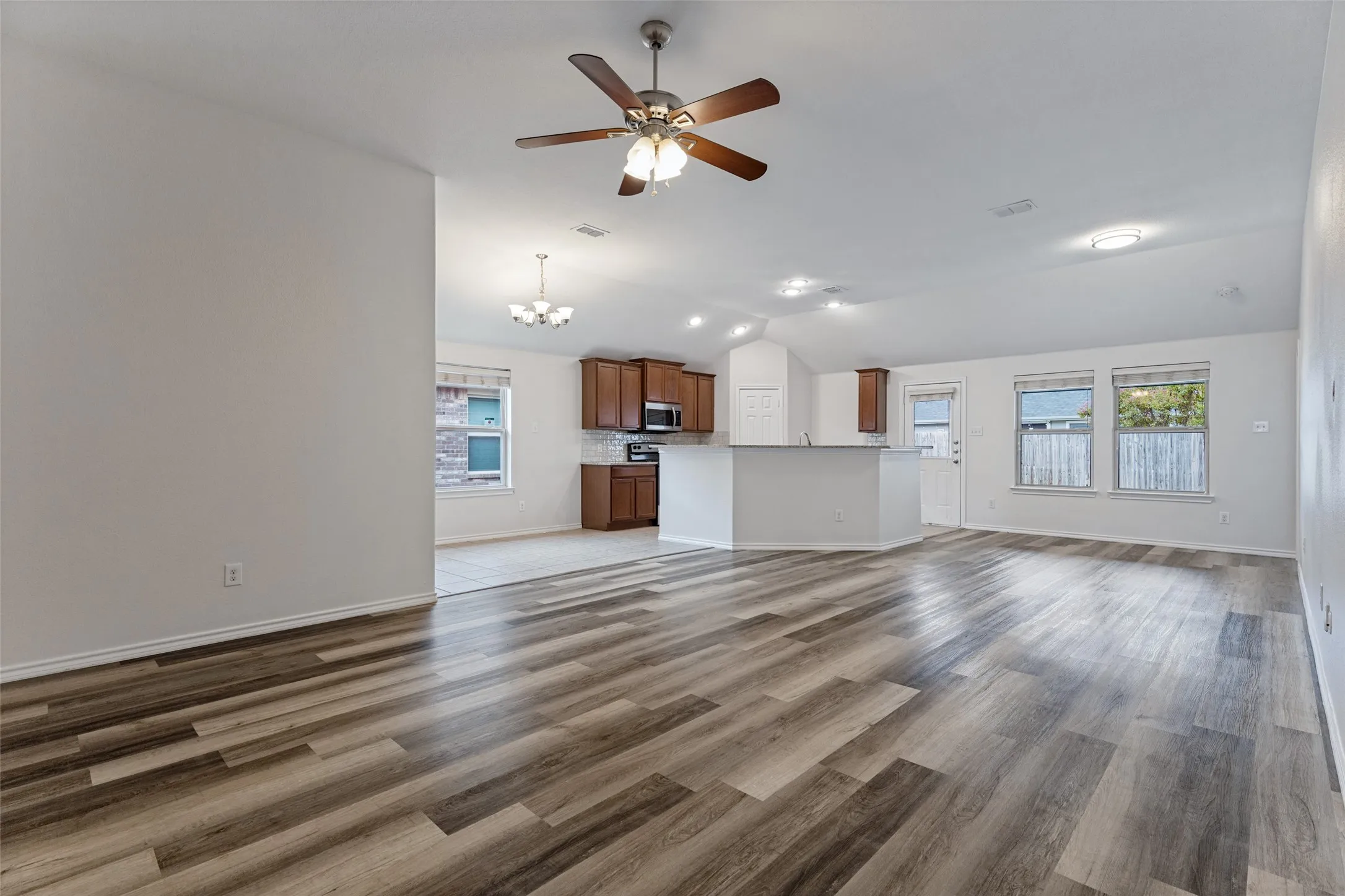 Open-concept living area showcasing engineered wood-finish flooring throughout, recessed ceiling lighting, and a ceiling fan with integrated light fixture