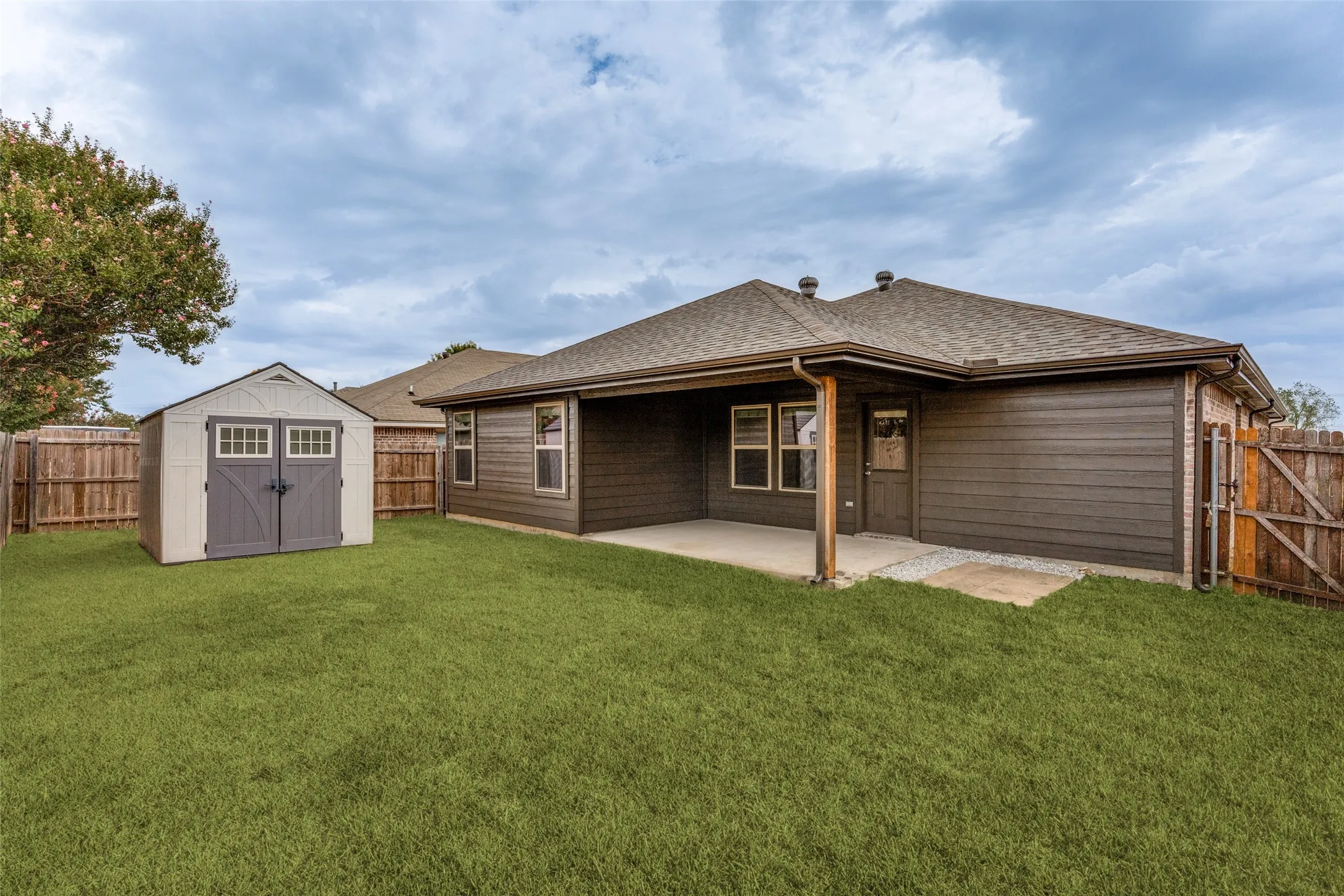 Expansive backyard featuring a manicured lawn, a covered patio, and a utility shed with double doors