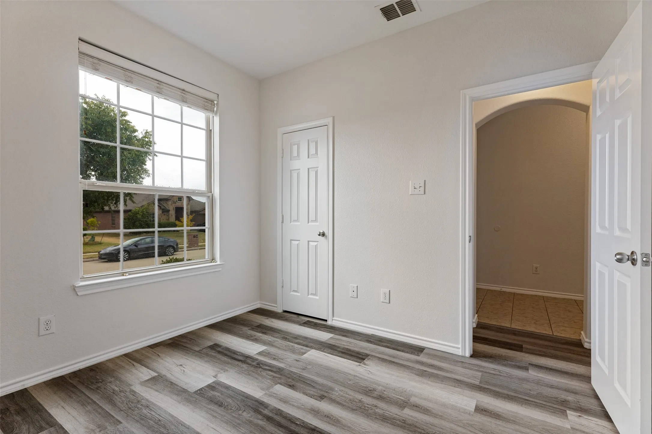 Room with wood-finish flooring, a white paneled door, and a multi-pane window