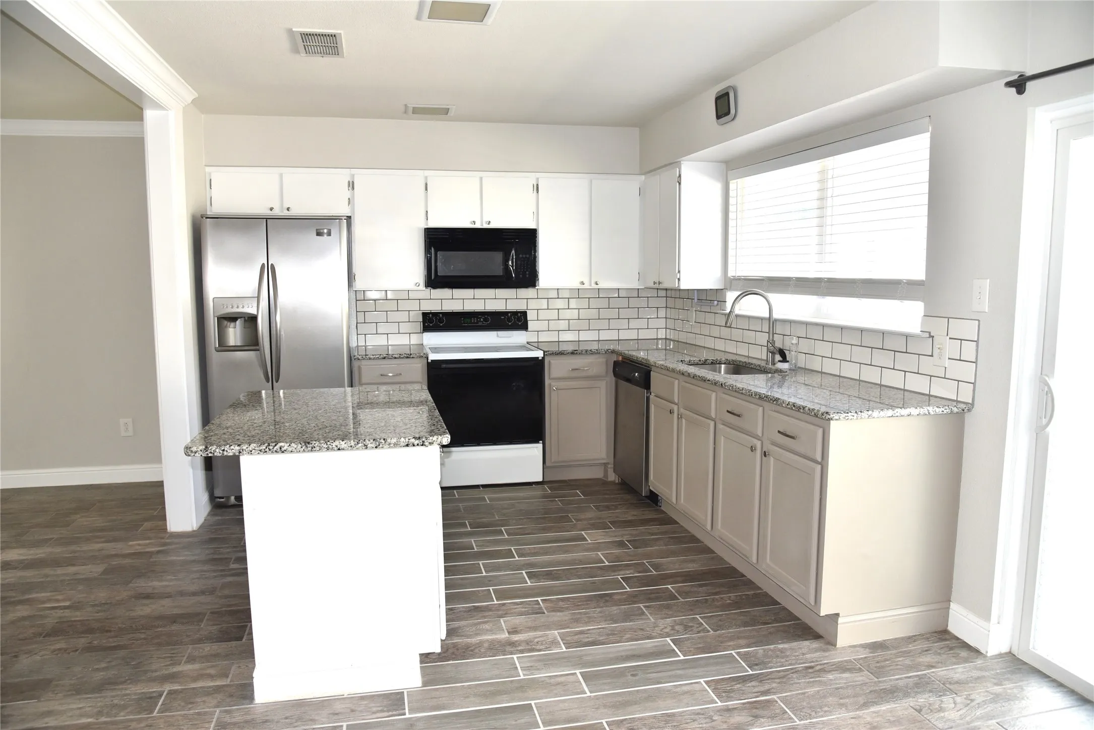 Kitchen featuring light stone countertops, appliances with stainless-steel refrigerator, ceramic tiled floors, decorative backsplash