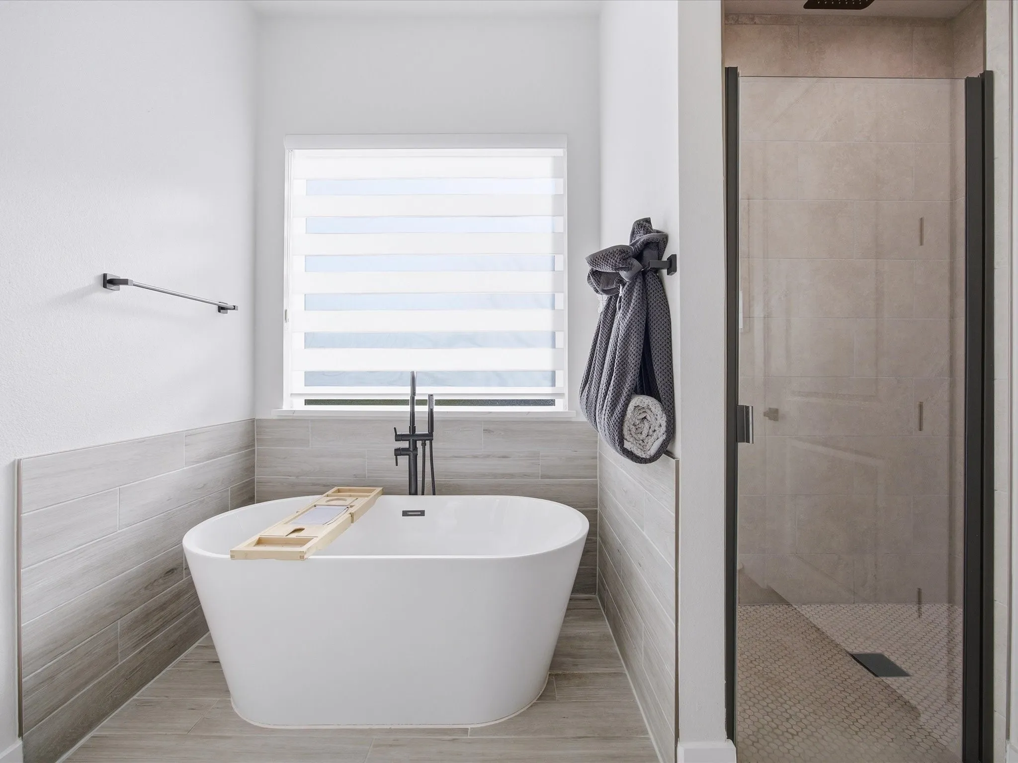 Full bathroom featuring tile walls, a shower stall, a soaking tub, and wainscoting