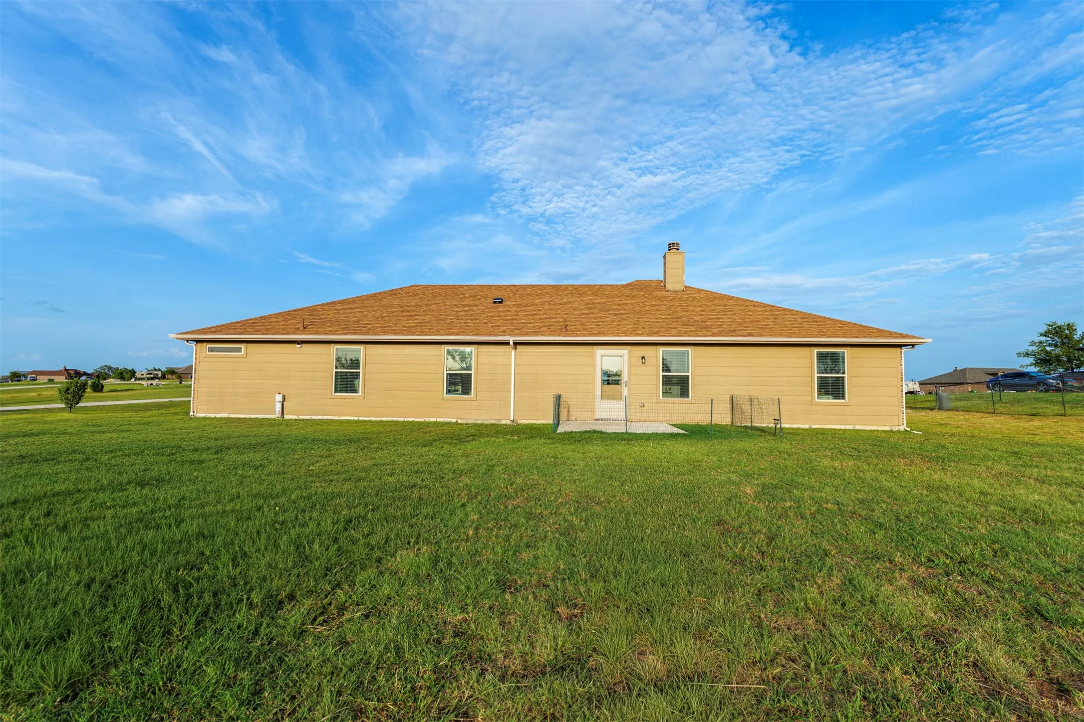 Expansive rear yard featuring a concrete patio, exterior lighting, and a single chimney