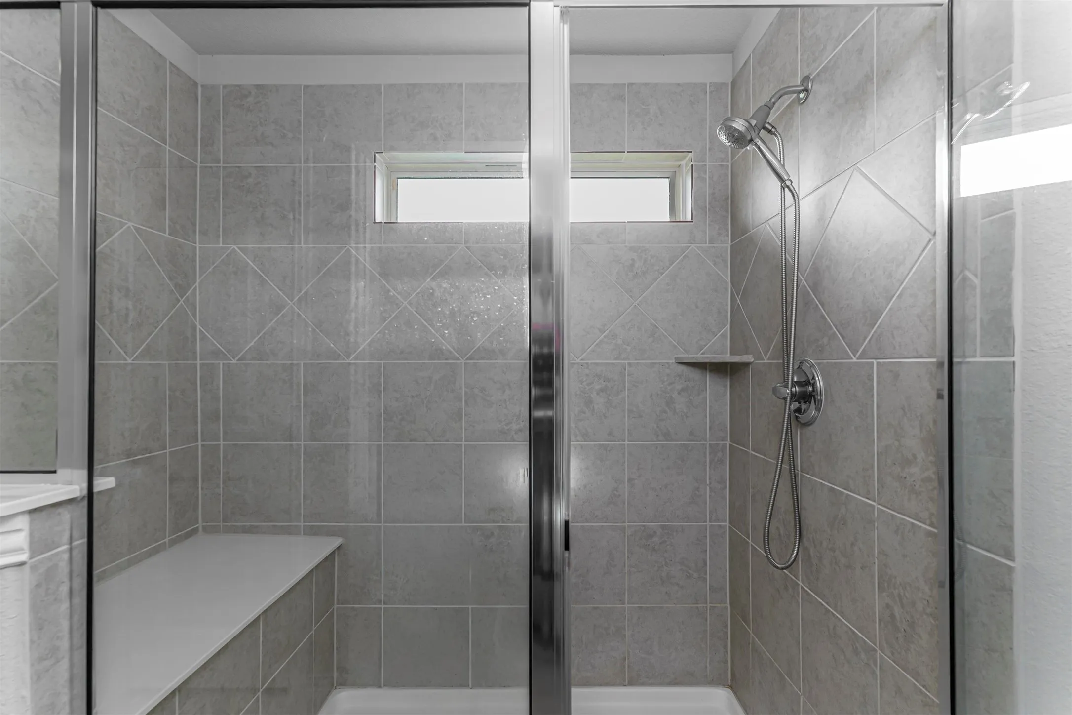 Tiled shower enclosure featuring a fixed window, built-in bench, and a handheld shower fixture