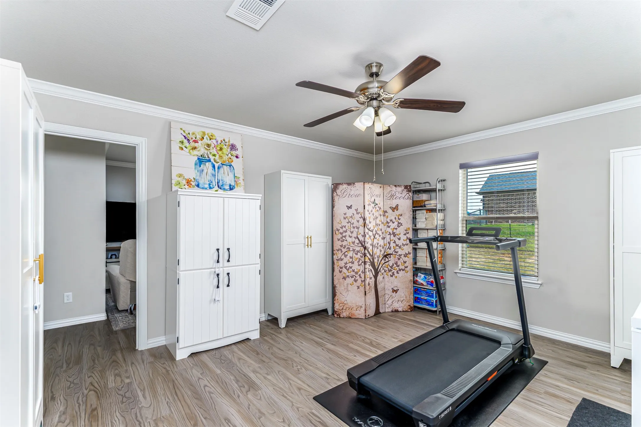 Wood-finish flooring throughout, white crown molding, and a ceiling fan with integrated lighting