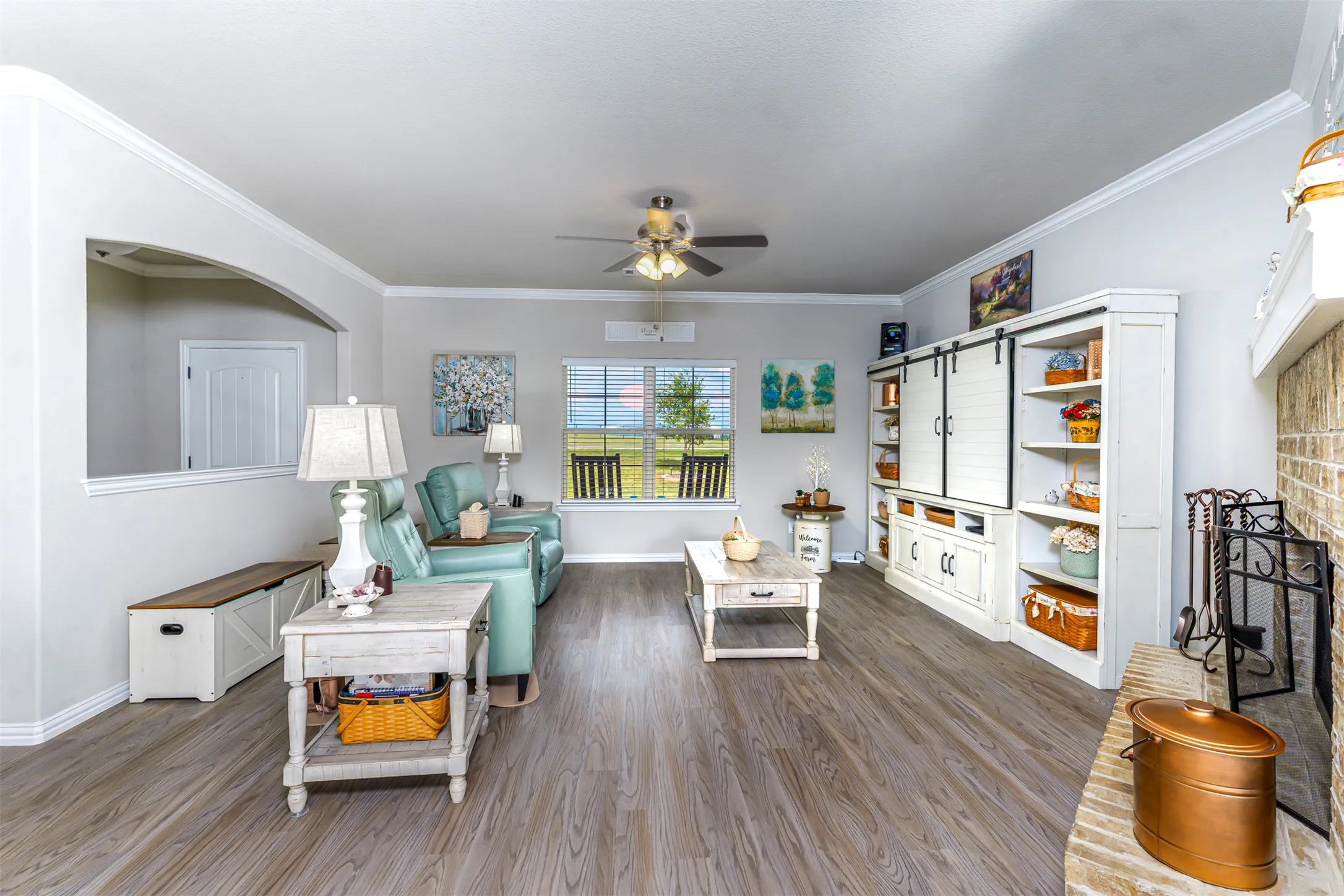 Wood-finish flooring, built-in entertainment center with barn door accents, ceiling fan, crown molding, and an arched half-wall opening