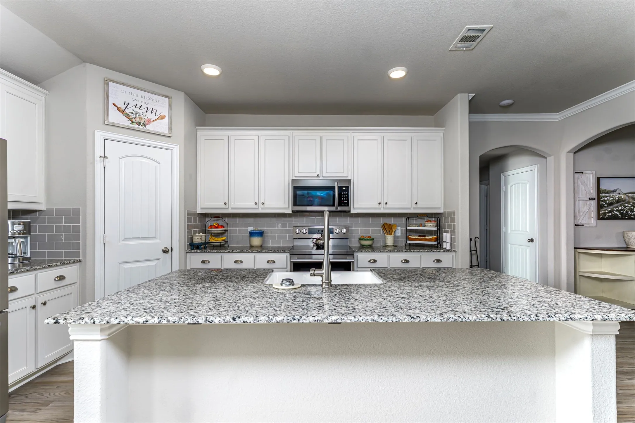 Kitchen island with integrated sink, white cabinetry, stainless steel appliances, tile backsplash, and recessed lighting