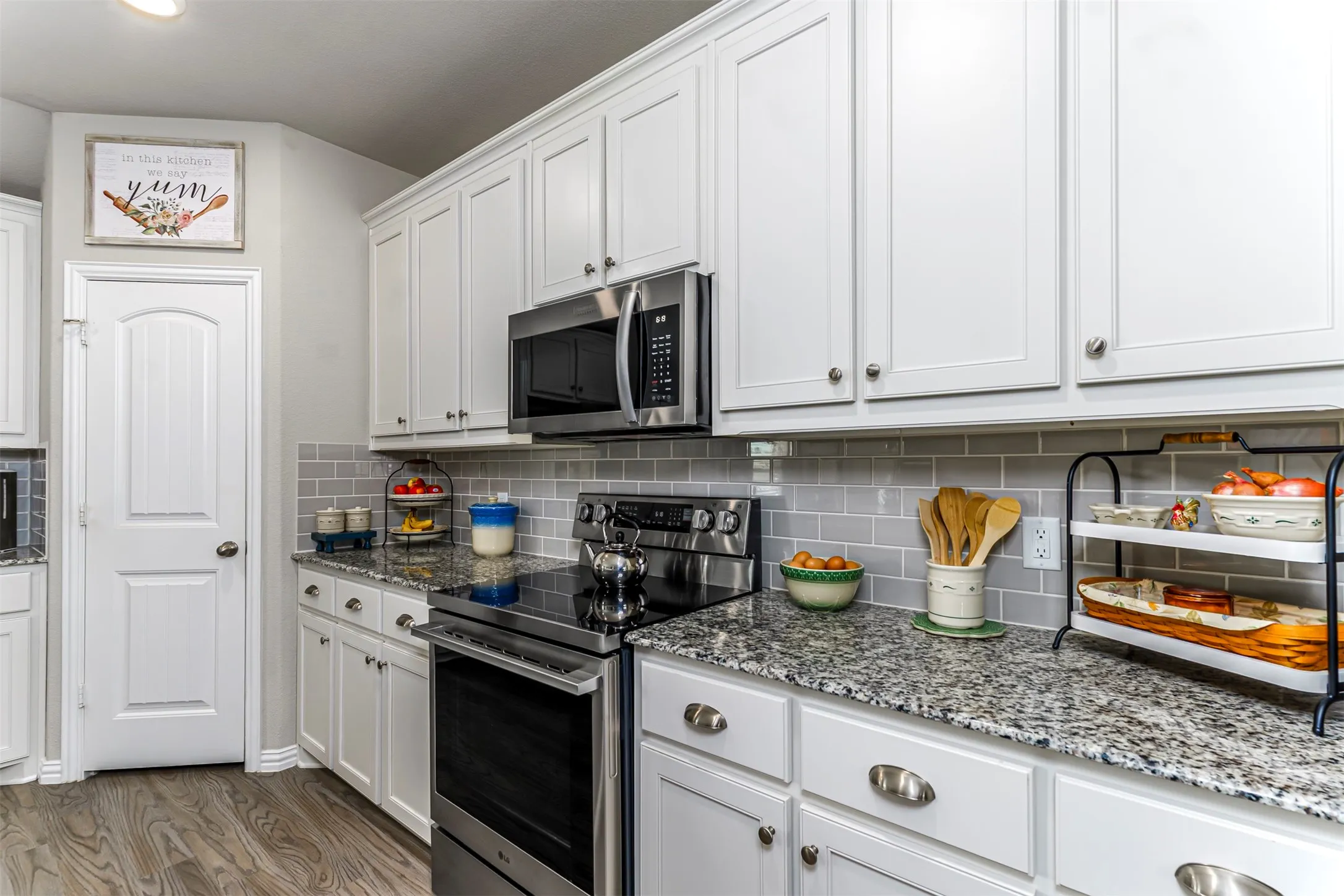 White shaker-style cabinetry, granite countertops, subway tile backsplash, stainless steel appliances, and wood-finish flooring