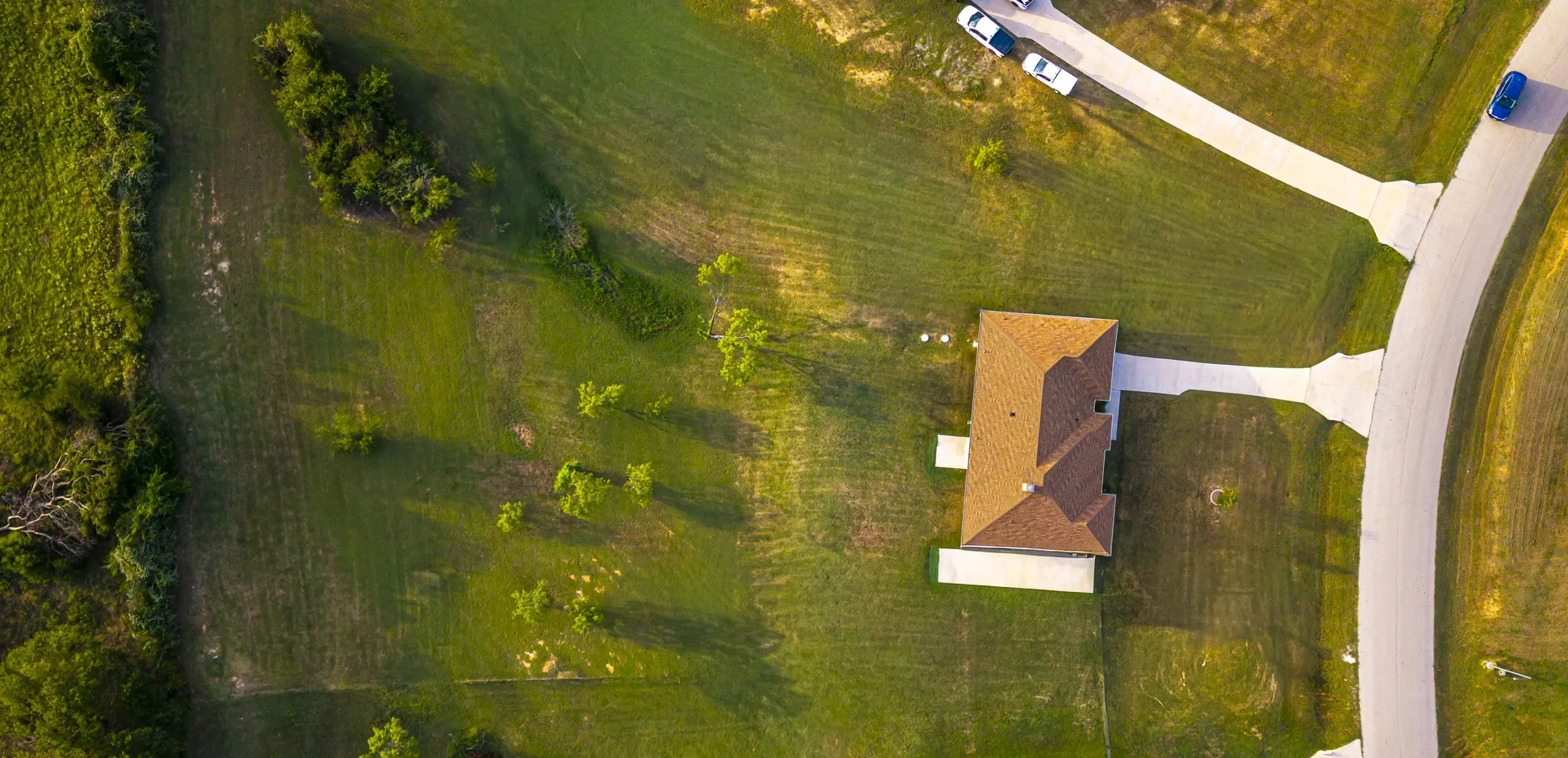 Aerial view showcasing a brick residence sited on expansive grounds with mature landscaping, a paved driveway, and open lawn space