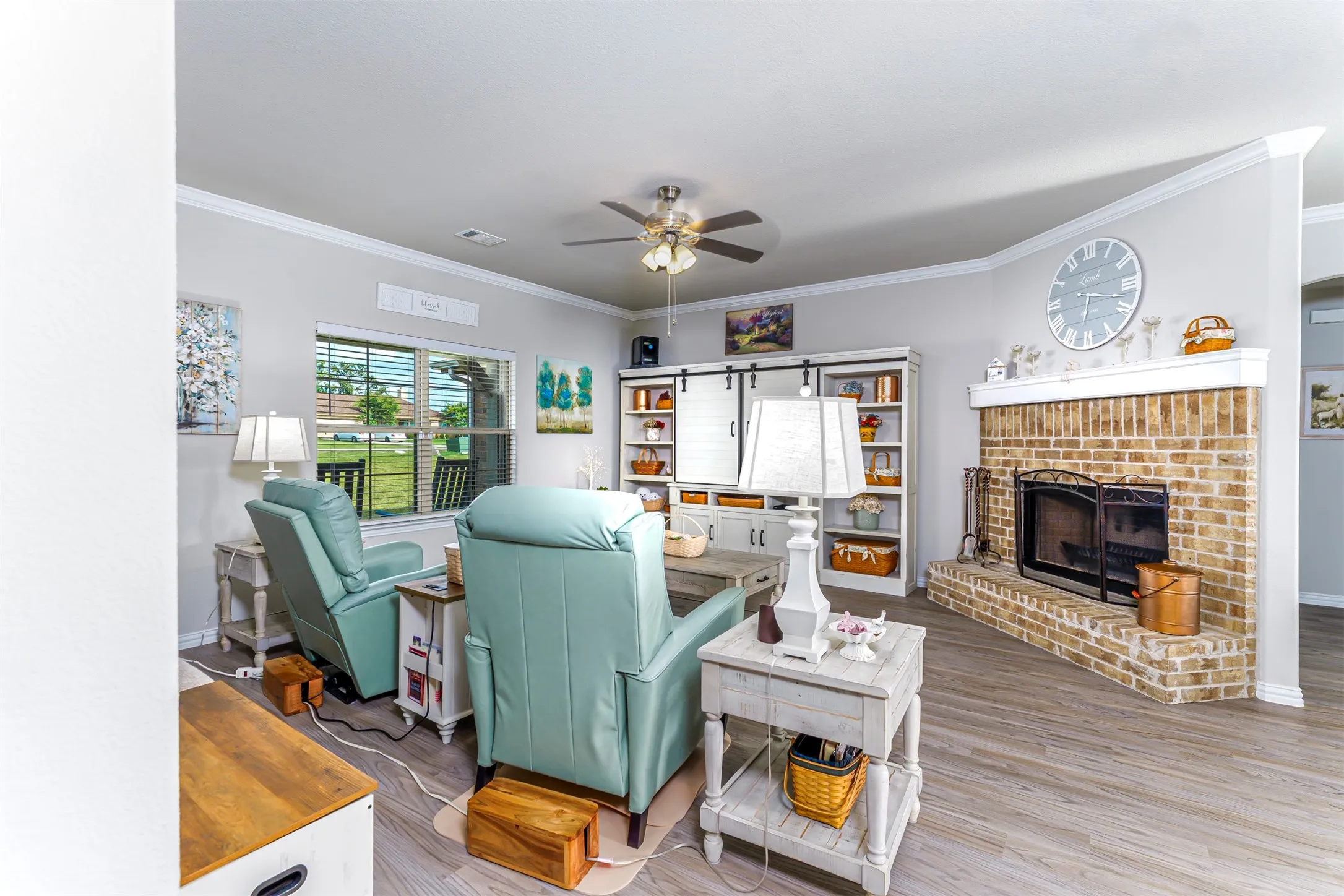 Corner brick fireplace with a raised hearth, built-in shelving with barn door accents, ceiling fan, and wood-finish flooring