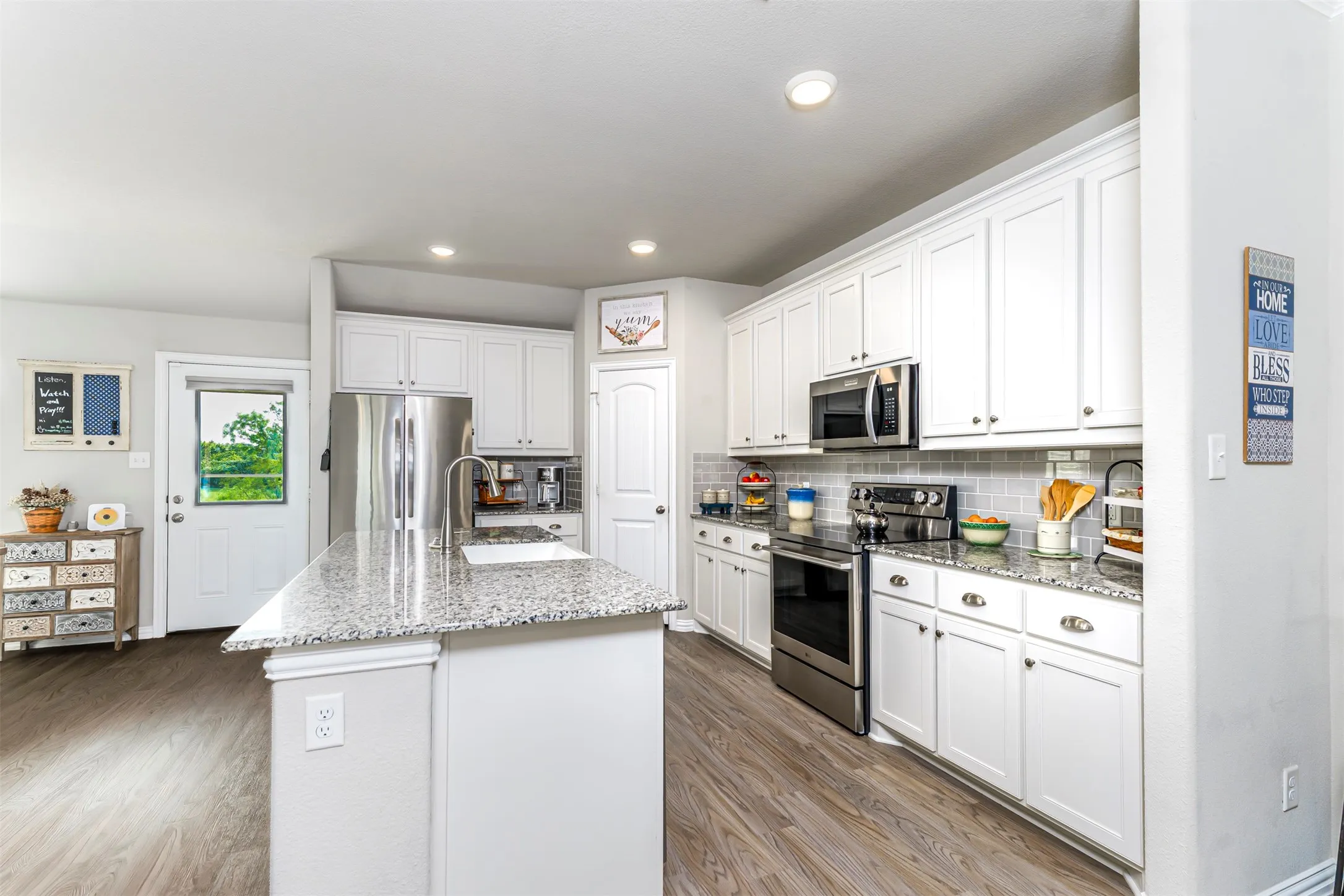 Kitchen featuring white cabinetry, stainless steel appliances, granite countertops, a center island with sink, and wood-finish flooring