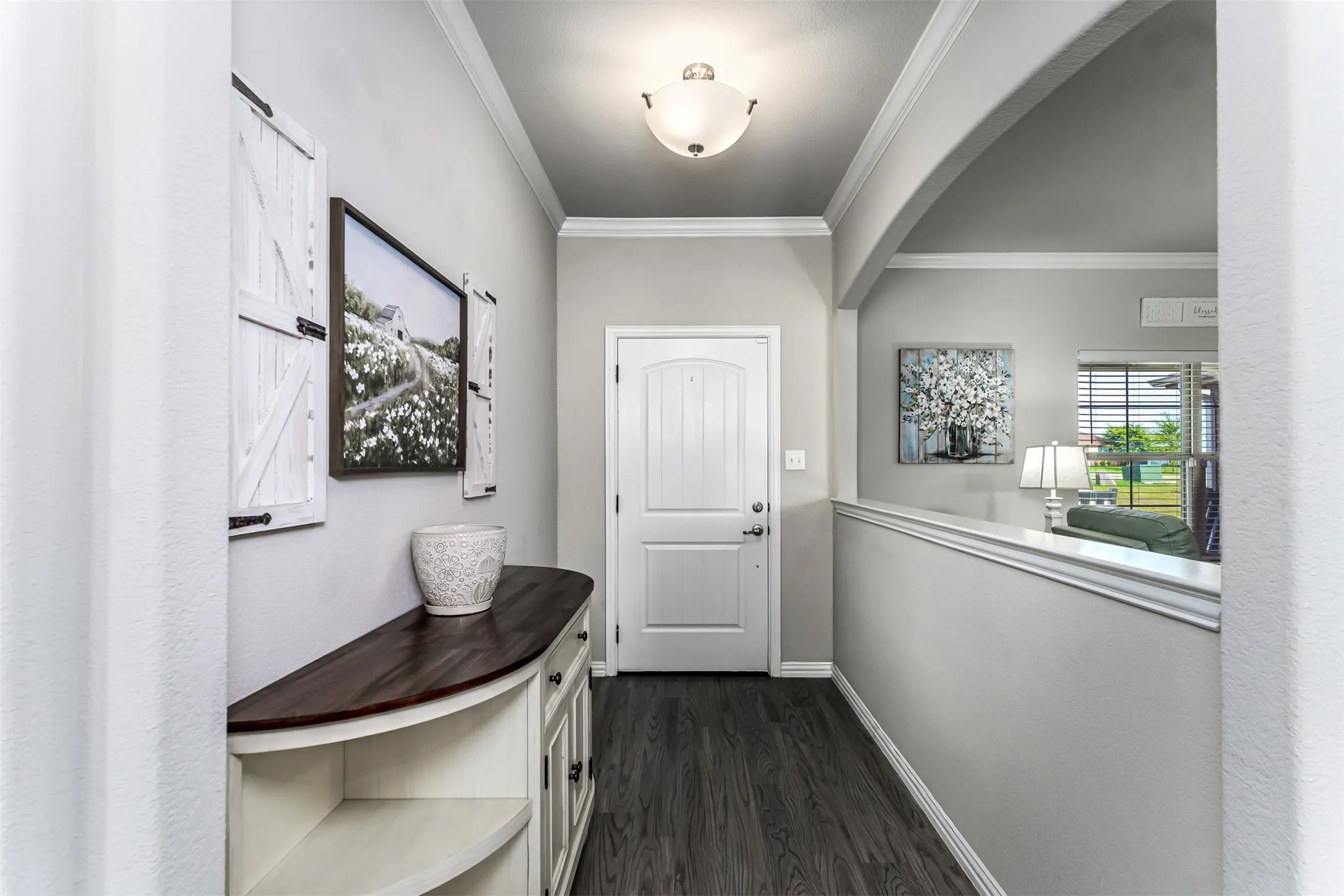 Arched entryway with crown molding, wood-finish flooring, and a paneled white door