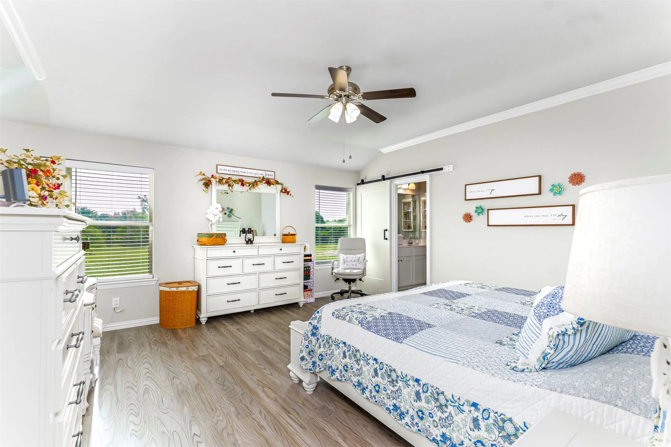 Vaulted ceiling with a ceiling fan, wood-finish flooring, two windows with blinds, and an interior barn door