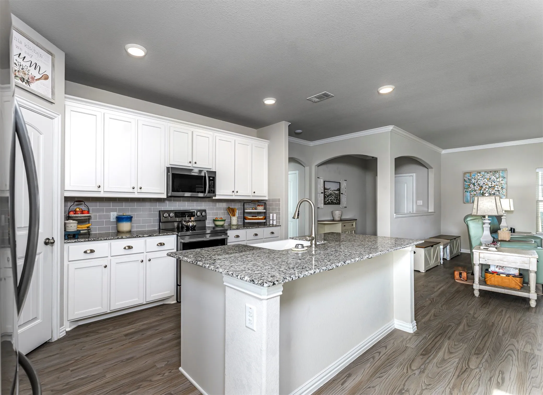 Kitchen featuring white cabinetry, grey subway tile backsplash, stainless steel appliances, a large island with a sink, and wood-finish flooring