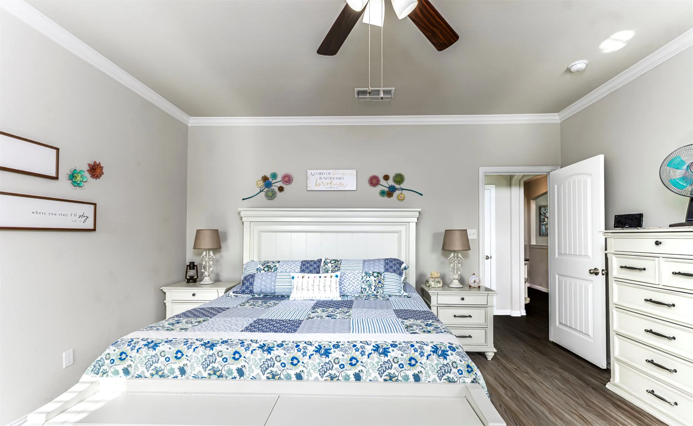 Bright primary bedroom showcasing a white shaker-style headboard with integrated storage, wood-finish flooring, ceiling fan with integrated lighting, recessed ceiling lights, and direct access to an ensuite bathroom and walk-in closet