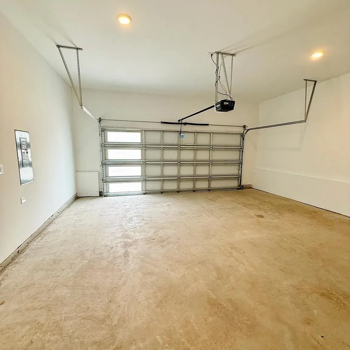 Spacious garage featuring a sectional door with frosted rectangular window panels, an automatic garage door opener, and overhead lighting