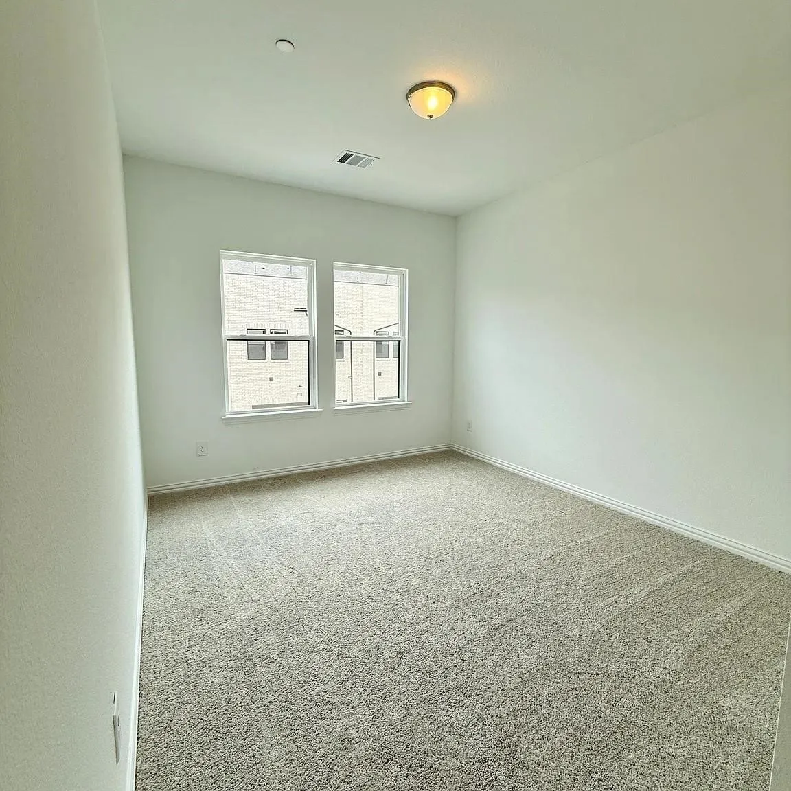 Neutral tone carpeting, two windows, and overhead lighting