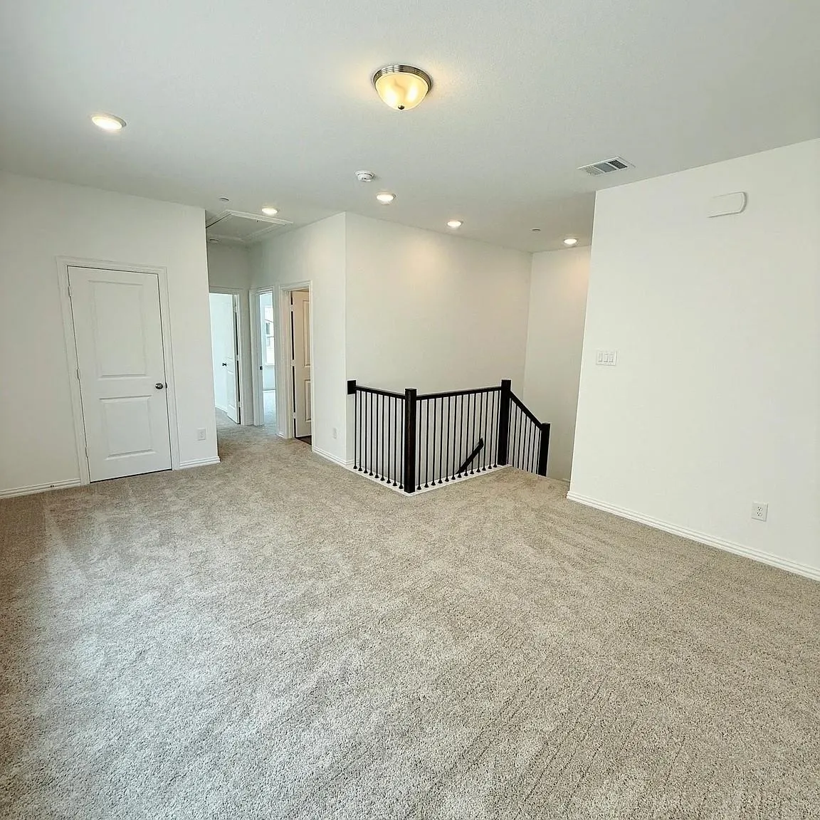 Expansive carpeted area featuring recessed lighting, a semi-flush mount light fixture, and a black metal spindle railing
