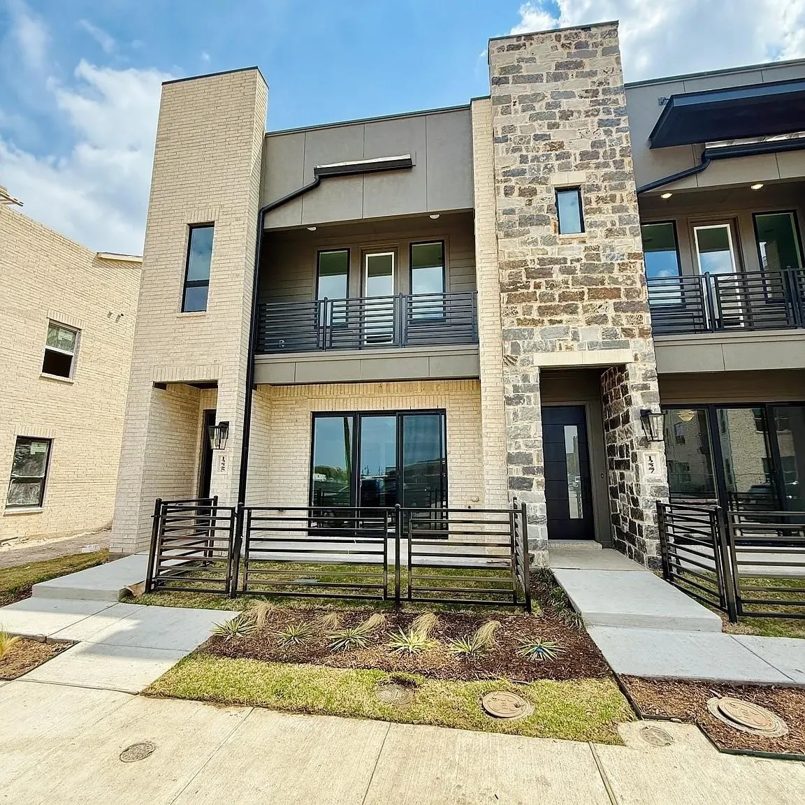 Modern townhouse with a multi-level facade, featuring a stone and brick exterior, black-framed windows, and metal balcony railings