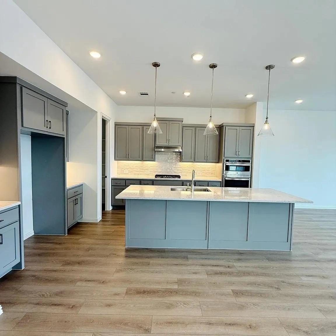 Kitchen featuring gray cabinetry, a large center island with a sink, stainless steel appliances, and wood-finish flooring