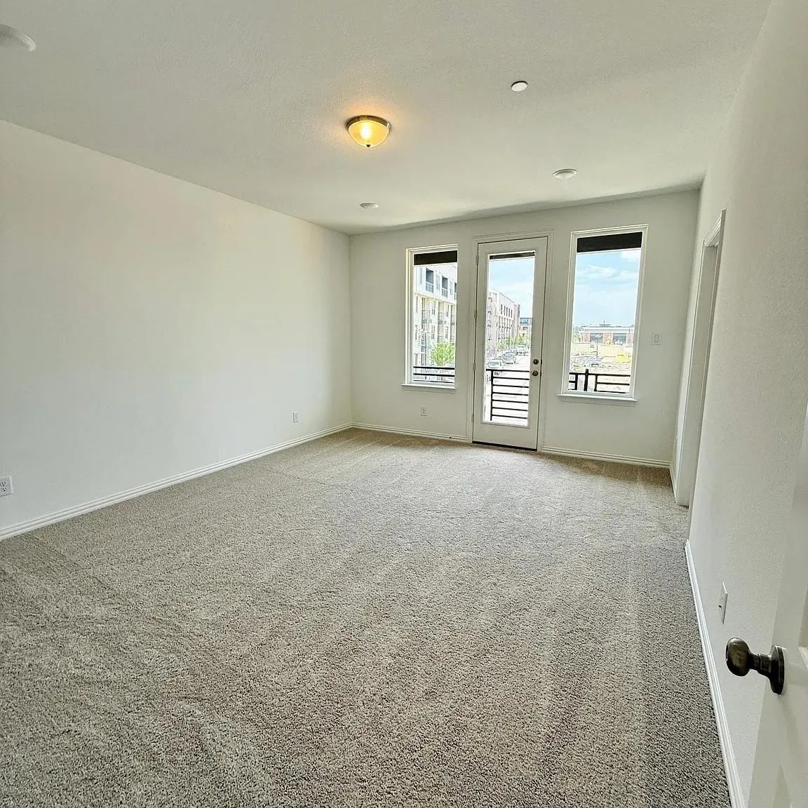 Wall-to-wall carpeting, white painted walls, recessed ceiling lighting, and a glass-paneled door with a metal railing balcony