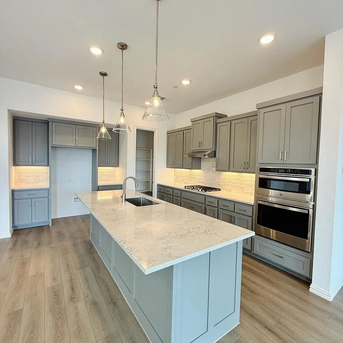 Open-concept kitchen featuring an expansive island with a stainless steel sink, wood-finish flooring, recessed lighting, and a built-in oven and microwave combination