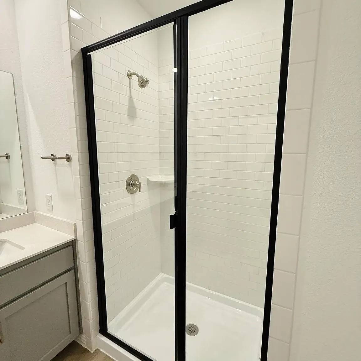Enclosed shower with subway tile surround, black-framed glass door, and brushed nickel fixtures