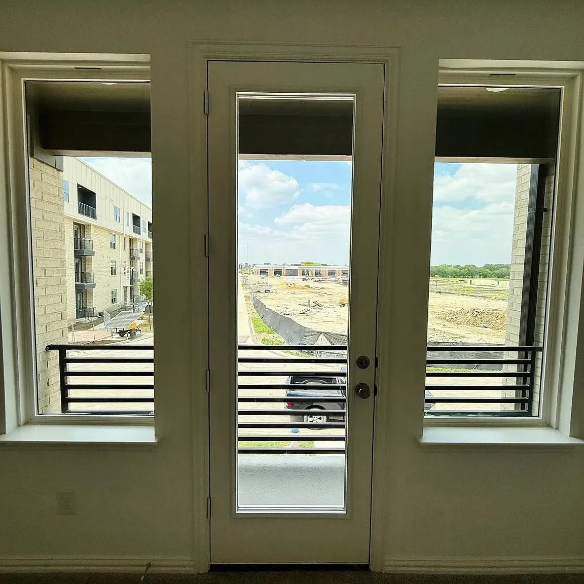 Full-light glass panel door flanked by two side windows, each with a black horizontal metal railing