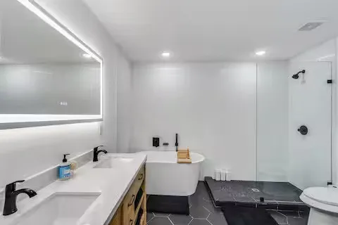 Dual-sink vanity with matte black fixtures, an illuminated mirror, and a freestanding soaking tub