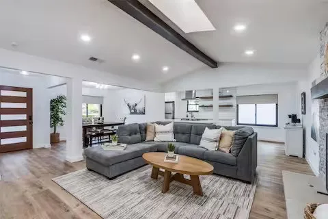 Wood-finish flooring throughout, vaulted ceiling with exposed beam, recessed lighting, and a modern entry door with horizontal glass panels