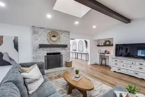 Vaulted ceiling with exposed beam, recessed lighting, skylight, stone-clad fireplace with hearth, and wood-finish flooring